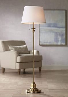 a floor lamp with a white shade on it and a chair in front of it