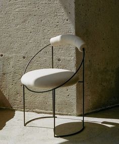 a white chair sitting on top of a metal stand next to a cement wall with holes in it