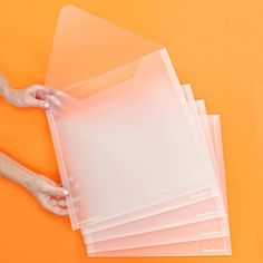 a person holding some clear plastic sheets on top of an orange surface