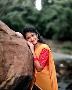 a woman leaning against a rock with trees in the background