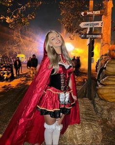 a woman dressed as a red riding hood and cape standing in front of a street sign