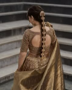 a woman in a gold sari walking down some steps with her back to the camera