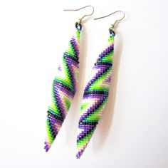 two pairs of beaded earrings with green, purple and white designs on them sitting side by side