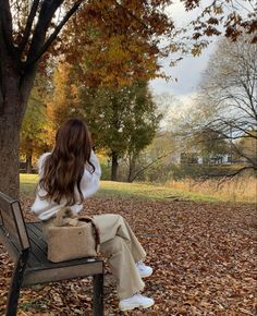 a woman is sitting on a bench in the park with autumn leaves all around her