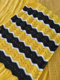 a yellow and black crocheted blanket sitting on top of a bed next to a pillow