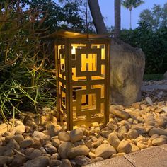 a lantern is sitting on some rocks in the middle of a garden with trees and bushes behind it