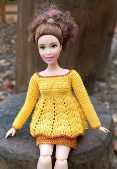 a doll sitting on top of a rock wearing a yellow crocheted dress and pink shoes