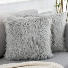 two gray pillows sitting on top of a grey couch next to a potted plant