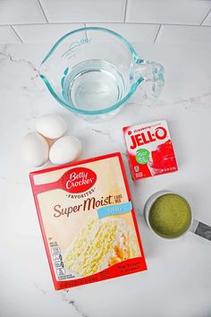 ingredients to make cake sitting on top of a white marble counter next to a measuring cup