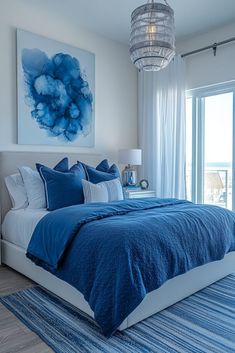 a blue and white bedroom with a chandelier hanging above the bed in front of a large window