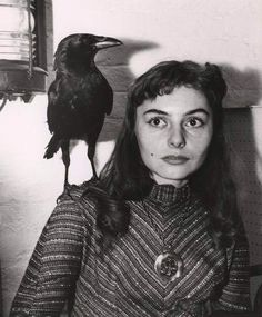 a black and white photo of a woman with a crow on her head next to a window