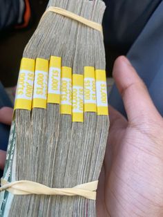 a person holding four bundles of money in their left hand, with yellow tape on them