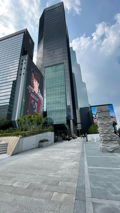 two tall buildings with large windows in the middle of a city square, one building has a giant screen on it's side