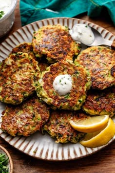 several crab cakes on a plate with lemon wedges and sour cream in the background