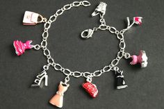 A collection of silver plated and colorfully enameled fashion themed charms have been dispersed around a shimmering silver plated bracelet chain in this handmade charm bracelet. This fashion charm bracelet is then completed with a lobster clasp and a 1/2 inch of chain at the end for adjustable sizing. Charms in this bracelet include three enameled pink dress charms, an enameled black dress charm, two enameled shoe charms, two enameled purse charms, and a detailed corset charm. ● Sizing ● To dete Handmade Metal Charm Bracelet For Parties, Trendy Silver Charm Bracelet With Dangling Charms, Silver Charm Bracelets As Fashion Accessory, Silver Charms Bracelet As Fashion Accessory, Silver Bracelets With Charms As Fashion Accessory, Trendy Silver Bracelet Charms, Trendy Silver Enamel Jewelry, Trendy Silver Charm Bracelet With Removable Charms, Trendy Nickel-free Silver Charms