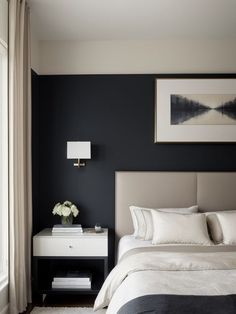 a bedroom with black walls, white bedding and an art work on the wall