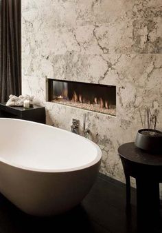 a large white bath tub sitting next to a fire place in a bathroom under a window