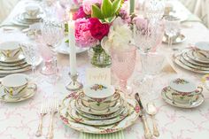 the table is set with pink and white flowers in vases, plates, silverware, and candlesticks