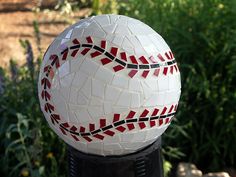 a mosaic ball sitting on top of a black pole in front of some bushes and flowers