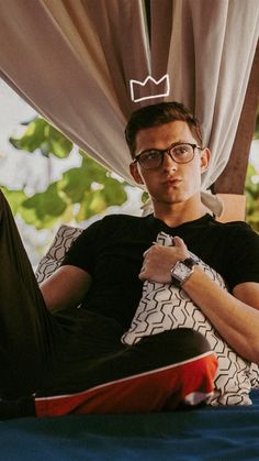 a man with glasses and a crown on his head is sitting in a bed looking at the camera