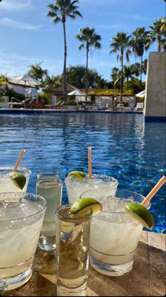 three glasses filled with drinks next to a swimming pool