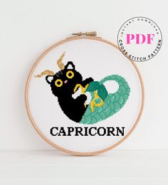 a black cat with horns on it's head and the word capricorn is in front of a cross - stitch hoop