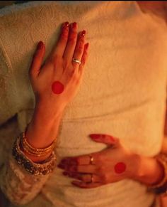 a woman with red painted hands on her belly and wearing gold bracelets, sitting in bed