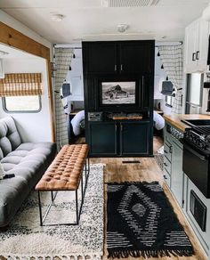 a living room and kitchen area in a mobile home with wood floors, white cabinets, black appliances, and rugs