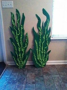 two large green plants sitting next to each other on a tile floor in front of a window