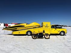 a yellow truck with a boat on it's back in the middle of snow