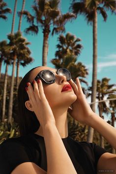 a woman wearing sunglasses and holding her hands to her face with palm trees in the background