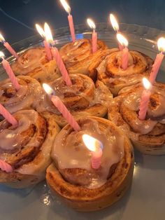 there are many cinnamon rolls with candles in the middle on a glass platter that is ready to be eaten