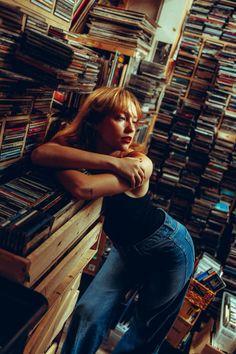 a woman leaning on a wooden table in front of a large amount of records and cds