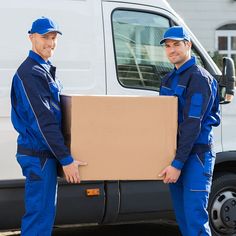 two men in blue work clothes are holding a cardboard box next to a white van