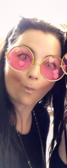 a woman with pink heart shaped glasses on her face and long black hair, is taking a selfie