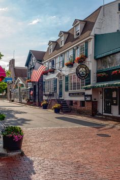 an empty street lined with shops and flowers in front of them on a sunny day