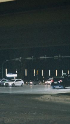 cars are driving down the street in front of an overpass with traffic lights at night