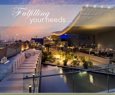 an outdoor walkway next to a body of water at dusk with lights shining on the building