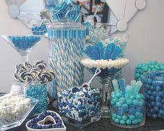 a table topped with lots of blue and white candies next to a tall glass vase filled with lollipops