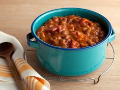 a blue bowl filled with baked beans next to a spoon