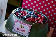 a green bowl filled with lots of candy on top of a table next to a cup