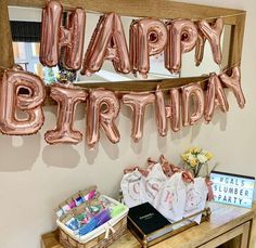 a birthday party with pink balloons and gifts on a table in front of a sign that says happy birthday