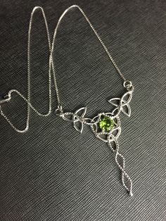 "I've designed this long, statement Celtic inspired necklace entirely in sterling silver featuring a center, faceted 10x8mm peridot gemstone! The frame, or centering, of the pendant is made with Celtic Trinity Knots and sterling wire work braids down the center to add the balancing touches to the piece. It comes with a sterling box chain which is soldered to each end of the pendant. This piece is 18\" in length, including the chain, and the pendant, itself, is approximately 3 inches, in height, Silver Peridot Jewelry As Gift, May Birthstone Jewelry In Silver With Peridot, Silver Peridot Jewelry For May Birthstone, Silver Peridot Jewelry For Anniversary, Silver Peridot Jewelry With Gemstone, Silver Peridot Birthstone Jewelry, Formal Peridot Jewelry For May Birthstone, Elegant Peridot Jewelry For May Birthstone, Elegant Peridot Necklaces For Wedding