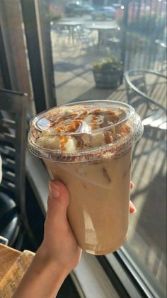 a person holding up a drink in front of a window