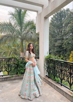 a woman in a blue and pink lehenga standing on a balcony with palm trees