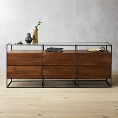 a wooden dresser with glass top and drawers on the bottom, in front of a white wall