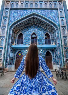 a woman in a blue and white dress is standing in front of an ornate building