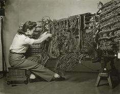 an old photo of a woman working on a large rack of electrical wires in a room