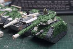 two toy tanks sitting on top of a green table next to a keyboard and mouse