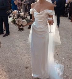 a woman in a white wedding dress holding a glass of wine and walking down the street